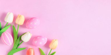 Mutlu Paskalya bayramı tebrik kartı konsepti. Renkli Paskalya yumurtaları ve pastel pembe arka planda bahar çiçekleri. Üst görünüm, düz görünüm, kopyalama alanı.