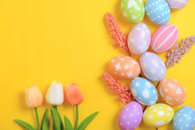 Mutlu Paskalya bayramı tebrik kartı konsepti. Sarı arka planda renkli Paskalya yumurtaları ve bahar çiçekleri. Üst görünüm, düz görünüm, kopyalama alanı.