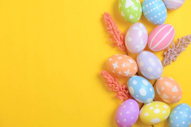 Mutlu Paskalya bayramı tebrik kartı konsepti. Sarı arka planda renkli Paskalya yumurtaları ve bahar çiçekleri. Üst görünüm, düz görünüm, kopyalama alanı.