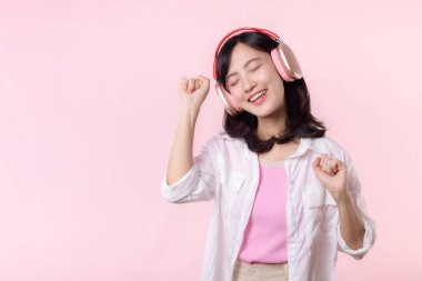 Gülümseyen Asyalı güzel model şarkı dinler ve kablosuz kulaklıkla internetteki müzik radyosunun tadını çıkarır. Pozitif eğlence, pembe izole edilmiş arka plan stüdyosundaki neşeli genç kadın.