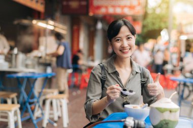 Mutlu genç Asyalı kadın sırt çantası gezgini Bangkok, Tayland 'daki Çin şehir marketinde sokak yemekleri yiyor..