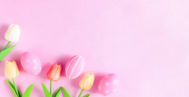 Mutlu Paskalya bayramı tebrik kartı konsepti. Renkli Paskalya yumurtaları ve pastel pembe arka planda bahar çiçekleri. Üst görünüm, düz görünüm, kopyalama alanı.