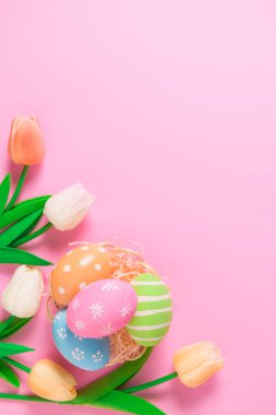 Mutlu Paskalya bayramı tebrik kartı konsepti. Renkli Paskalya yumurtaları ve pastel pembe arka planda bahar çiçekleri. Üst görünüm, düz görünüm, kopyalama alanı.