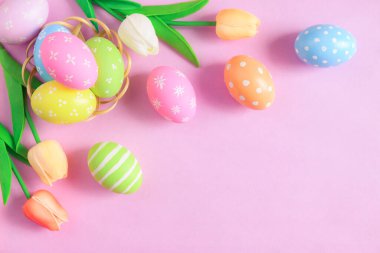 Mutlu Paskalya bayramı tebrik kartı konsepti. Renkli Paskalya yumurtaları ve pastel pembe arka planda bahar çiçekleri. Üst görünüm, düz görünüm, kopyalama alanı.