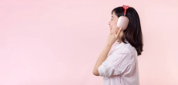 サイドビュー笑顔の若い陽気な楽しい女性彼女はピンクのシャツの白いTシャツのヘッドフォンを着用し 音楽に耳を傾けるプレーンパステルライトピンクの背景に隔離された携帯電話を使用しています 人々のライフスタイルコンセプト — ストック写真