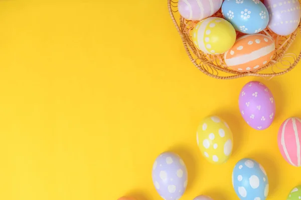 幸せなイースターお祝いの休日 カラフルなパステルは黄色の背景にウィッカーバスケット巣の装飾で卵を描いた 季節のグリーティングギフトカードコンセプト フラットレイアウト トップビュー コピースペース — ストック写真