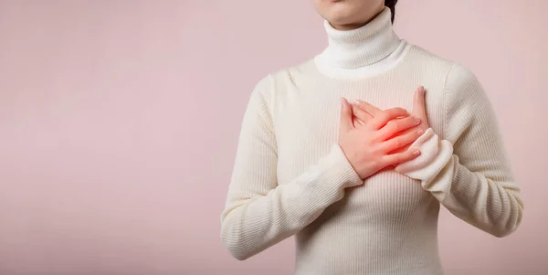 Young asian woman suffering from heart attack on light pink studio background. Painful cramps, Heart disease, Pressing on chest with painful expression. Healthcare concept.