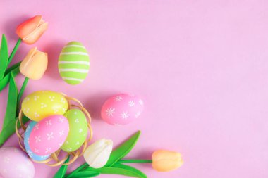Mutlu Paskalya bayramı tebrik kartı konsepti. Renkli Paskalya yumurtaları ve pastel pembe arka planda bahar çiçekleri. Üst görünüm, düz görünüm, kopyalama alanı.