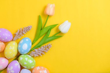 Mutlu Paskalya bayramı tebrik kartı konsepti. Sarı arka planda renkli Paskalya yumurtaları ve bahar çiçekleri. Üst görünüm, düz görünüm, kopyalama alanı.