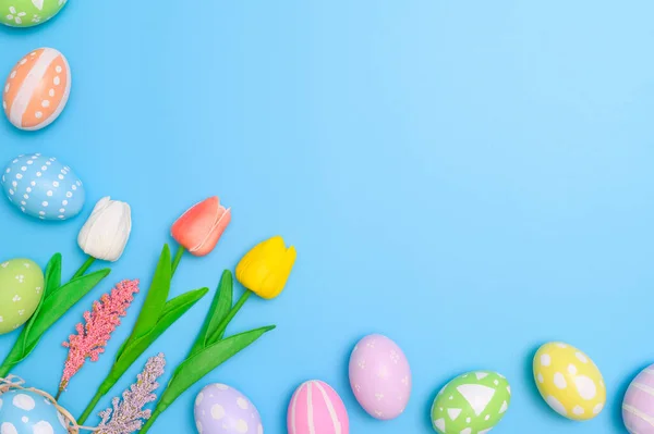 stock image Happy Easter holiday greeting card concept. Colorful Easter Eggs and spring flowers on blue background. Top view, flat lay, copy space.