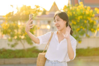 Portre güzel Asyalı kadın arkadaşlarıyla video görüşmesi yapmak ve yaz tatilinde Bangkok 'ta sokağı keşfetmek için akıllı telefon kullanıyor.