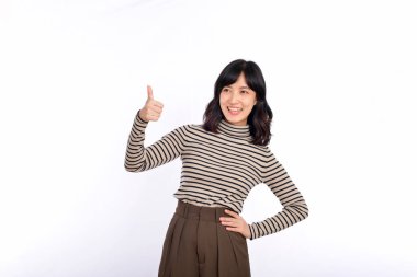 Süveter giyimli, kendine güvenen genç Asyalı kadın. Başparmağını göstererek onaylıyor, tavsiye ediyor, beyaz arka planda duruyor.
