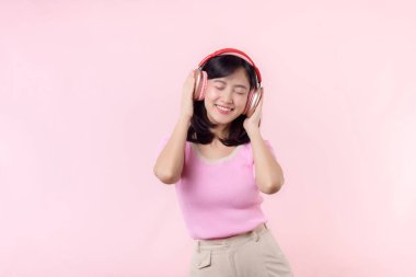 Gülümse güzel model, müzik dinle ve kablosuz kulaklıkla dansın tadını çıkar. Neşeli, neşeli bir genç kadın pembe izole edilmiş arka planda şarkı söylüyor.
