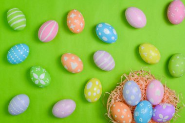 Mutlu Paskalya bayramı tebrik kartı konsepti. Renkli Paskalya yumurtaları ve pastel yeşil arka planda bahar çiçekleri. Üst görünüm, düz görünüm, kopyalama alanı.