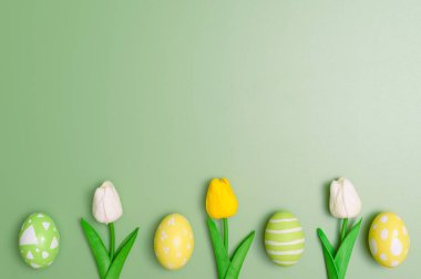 Mutlu Paskalya bayramı tebrik kartı konsepti. Renkli Paskalya yumurtaları ve pastel yeşil arka planda bahar çiçekleri. Üst görünüm, düz görünüm, kopyalama alanı.