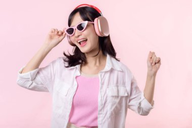 Moda güneş gözlüklü genç mutlu Asyalı kadın model pembe stüdyo arka planında izole edilmiş kulaklıkla müzik ve dans dinlemeyi seviyor. teknoloji, kız modası, aksesuar konsepti.