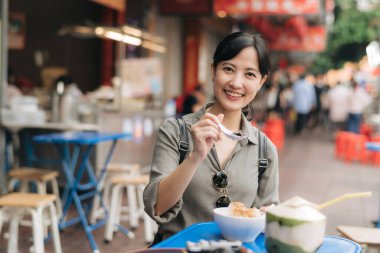 Mutlu genç Asyalı kadın sırt çantası gezgini Bangkok, Tayland 'daki Çin şehir marketinde sokak yemekleri yiyor..