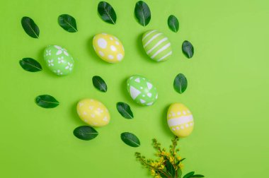 Mutlu Paskalya bayramı tebrik kartı konsepti. Renkli Paskalya yumurtaları ve pastel yeşil arka planda bahar çiçekleri. Üst görünüm, düz görünüm, kopyalama alanı.