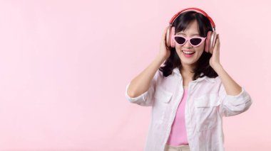 Moda güneş gözlüklü genç mutlu Asyalı kadın model pembe stüdyo arka planında izole edilmiş kulaklıkla müzik ve dans dinlemeyi seviyor. teknoloji, kız modası, aksesuar konsepti.