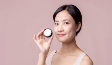 Yüz kremi sürmüş Asyalı genç bir kadın sağlıklı doğal cilt makyajında kozmetik nemlendirici. Parlak gülümsemeli kız modeli özenli güzellik ürünü, spa, kozmetoloji.