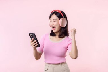 Portre genç, neşeli Asyalı kadın pembeye karşı akıllı telefon müzik uygulaması ile ses dinlemeyi seviyor. Kulaklıklı, mutlu, gülümseyen bir kadın. Ses, eğlence, yaşam tarzı, teknoloji konsepti