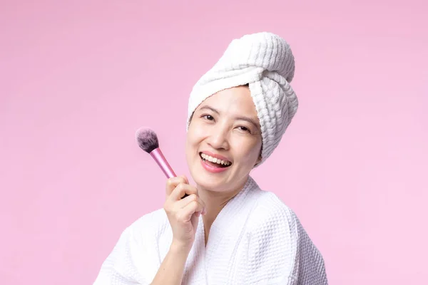 年轻快乐的亚洲女人 有着天生的妆容 有着粉红背景的化妆品皮肤粉红 女性使用护肤刷治疗 美容产品 化妆品学概念 — 图库照片