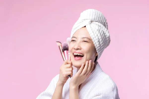 ピンクの背景に隔離された化粧品の皮膚パウダーブラッシャーを保持顔を構成する自然と肖像若い幸せなアジアの女性 女性はスキンケアブラシ治療を適用します 美容製品化粧品のコンセプト — ストック写真