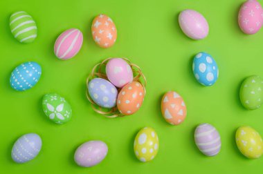 Mutlu Paskalya bayramı tebrik kartı konsepti. Renkli Paskalya yumurtaları ve pastel yeşil arka planda bahar çiçekleri. Üst görünüm, düz görünüm, kopyalama alanı.