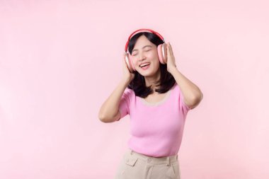 Gülümse güzel model, müzik dinle ve kablosuz kulaklıkla dansın tadını çıkar. Neşeli, neşeli bir genç kadın pembe izole edilmiş arka planda şarkı söylüyor.