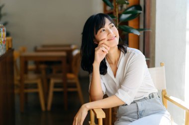 Brightly smiling beautiful young asian woman sitting in a coffee cafe in sunny day