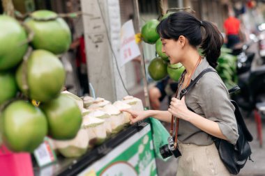 Mutlu Asyalı genç kadın sırt çantalı gezgin Bangkok, Tayland 'daki Çin mahallesi yiyecek pazarında hindistan cevizi suyu dükkanının önünde duruyor..