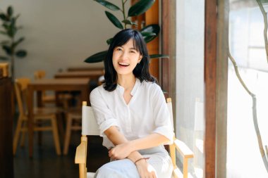 Brightly smiling beautiful young asian woman sitting in a coffee cafe in sunny day