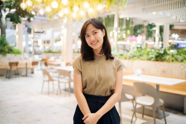 Smiling beautiful asian woman standing in cafeteria at shopping mall.