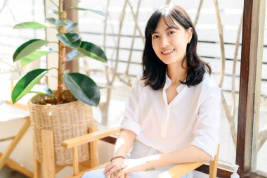 Brightly smiling beautiful young asian woman sitting in a coffee cafe in sunny day