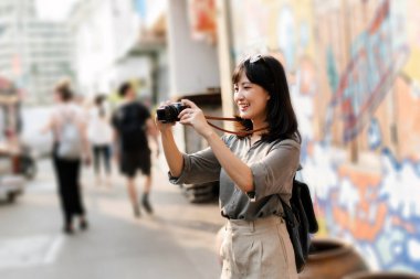 Young Asian woman backpack traveler using digital compact camera, enjoying street cultural local place and smile.