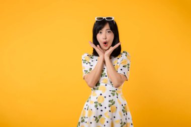 Portre genç çekici kendinden emin Asyalı kadın şaşırdı ve ağzını açtı. Sarı arka planda yalıtılmış bahar elbisesi ile ayakta duruyordu..