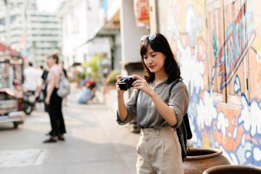 Young Asian woman backpack traveler using digital compact camera, enjoying street cultural local place and smile.
