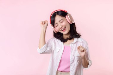 Gülümseyen Asyalı güzel model şarkı dinler ve kablosuz kulaklıkla internetteki müzik radyosunun tadını çıkarır. Pozitif eğlence, pembe izole edilmiş arka plan stüdyosundaki neşeli genç kadın.