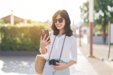 Portre güzel Asyalı kadın arkadaşlarıyla video görüşmesi yapmak ve yaz tatilinde Bangkok 'ta sokağı keşfetmek için akıllı telefon kullanıyor.