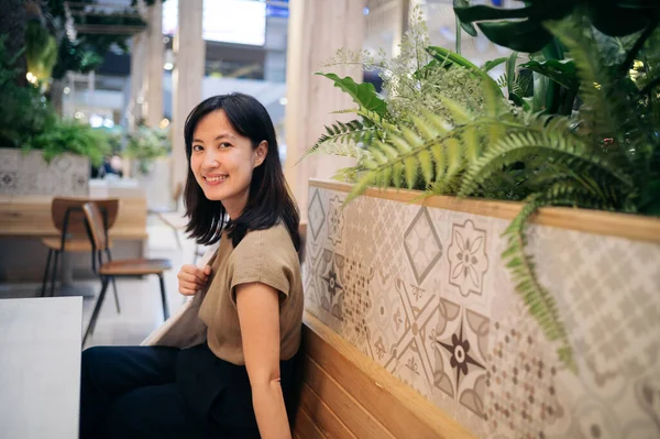 Smiling beautiful asian woman sitting in cafeteria at a shopping mall.