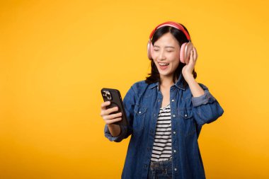 Portre genç, neşeli Asyalı kadın sarıya karşı akıllı telefon müzik uygulaması ile ses dinlemeyi seviyor. Kulaklıklı, mutlu, gülümseyen bir kadın. Ses, eğlence, yaşam tarzı, teknoloji konsepti
