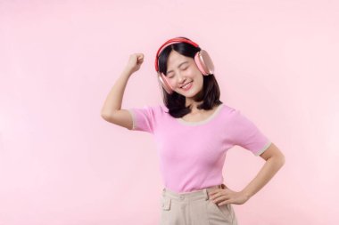 Gülümse güzel model, müzik dinle ve kablosuz kulaklıkla dansın tadını çıkar. Neşeli, neşeli bir genç kadın pembe izole edilmiş arka planda şarkı söylüyor.