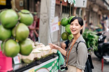 Mutlu Asyalı genç kadın sırt çantalı gezgin Bangkok, Tayland 'daki Çin mahallesi yiyecek pazarında hindistan cevizi suyu dükkanının önünde duruyor..