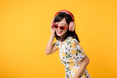 Gülümseyen Asyalı güzel model şarkı dinler ve kablosuz kulaklıkla internetteki müzik radyosunun tadını çıkarır. Pozitif eğlence, sarı izole edilmiş arka plan stüdyosundaki neşeli genç kadın.