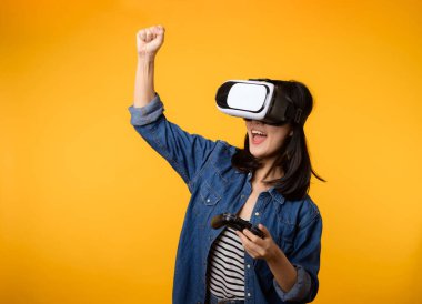 Asyalı genç bir kadın sanal gerçeklik kulaklığı takarak ve kumandayı sarı arka planda tutarak mutlu bir başarı elde etti. Sanal gelecek video oyunu konseptini kazanan.