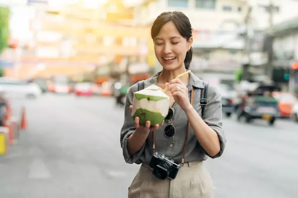 Stock image Happy young Asian woman backpack traveler drinking a coconut juice at China town street food market in Bangkok, Thailand.