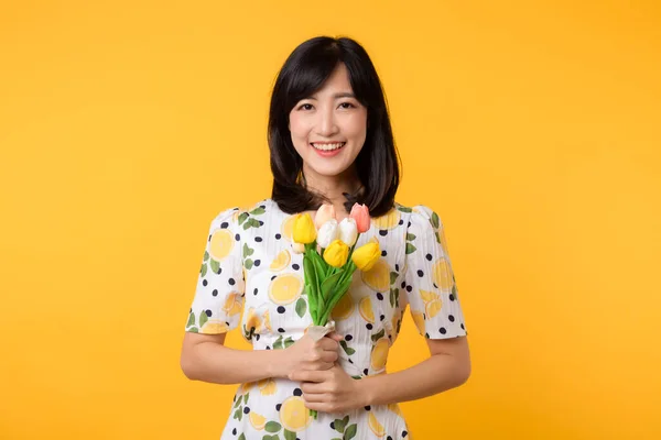 スタジオの肖像画かなり若いアジアの女性幸せな笑顔のドレッシング春のファッション黄色のスタジオの背景にチューリップ花束の花を保持 休日の概念 — ストック写真