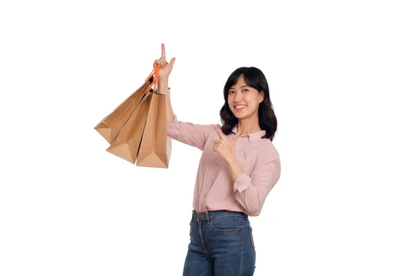 カジュアルなシャツとデニムジーンズを着た若い幸せなアジアの女性が白い背景に隔離されたショッピングペーパーバッグを保持 — ストック写真
