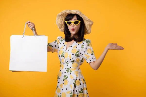 stock image Portrait attractive happy young asian woman with trendy springtime dress, hat, sunglasses fashion and paper bag isolated on yellow background. Summertime sale shopping concept.