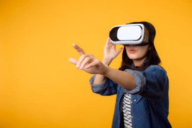 Asyalı genç bir kadın, sarı arka planda izole edilmiş sanal gerçeklik kulaklığı takmayı öğrenir. Sanal gelecek video oyunu konseptini kazanan.